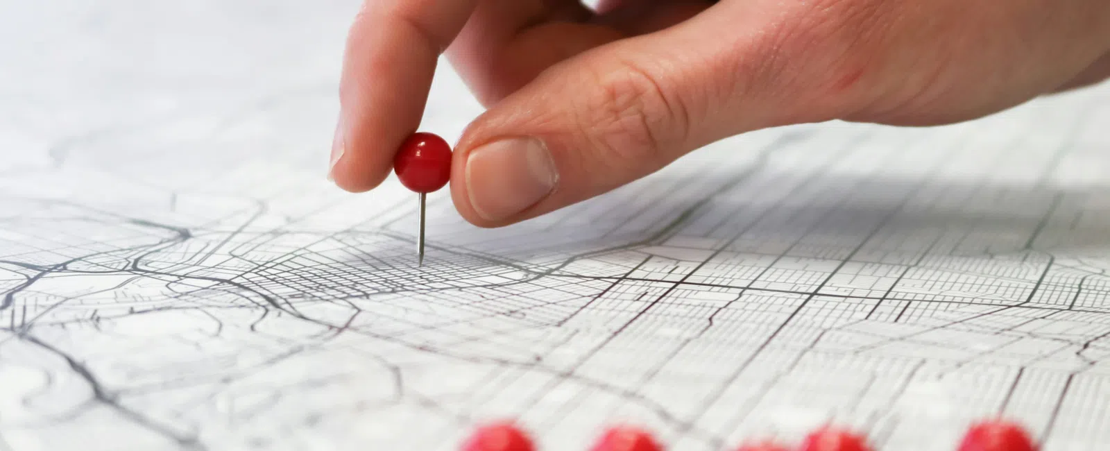 Hand placing a red pushpin on a detailed map with several red pushpins nearby.