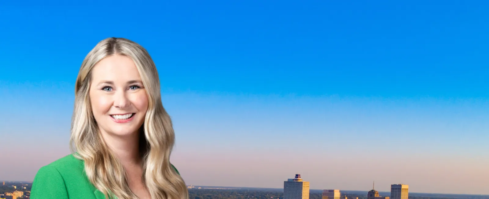 Smiling woman in green blazer stands before skyline and river view of Memphis, Tennessee with text about market of the month.