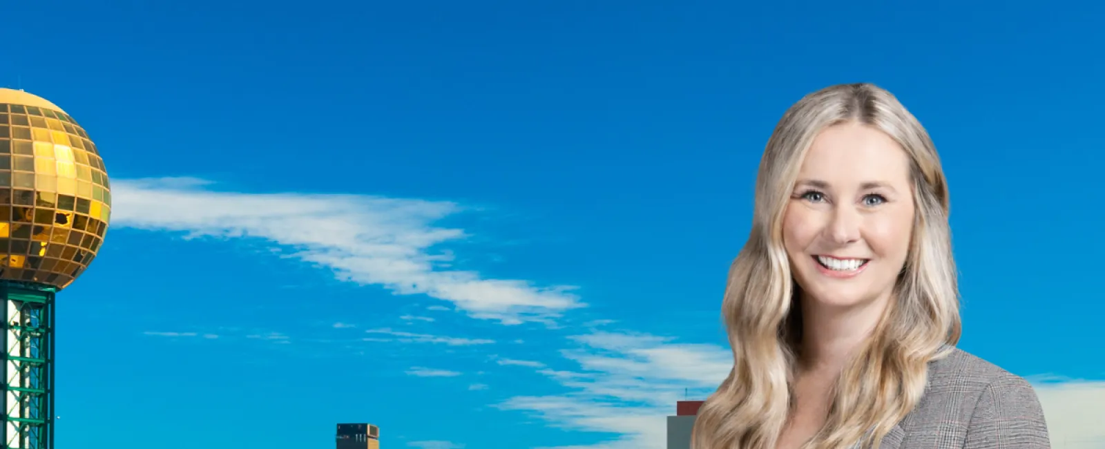 Smiling woman in blazer stands with Knoxville city skyline and Sunsphere tower in background on clear day