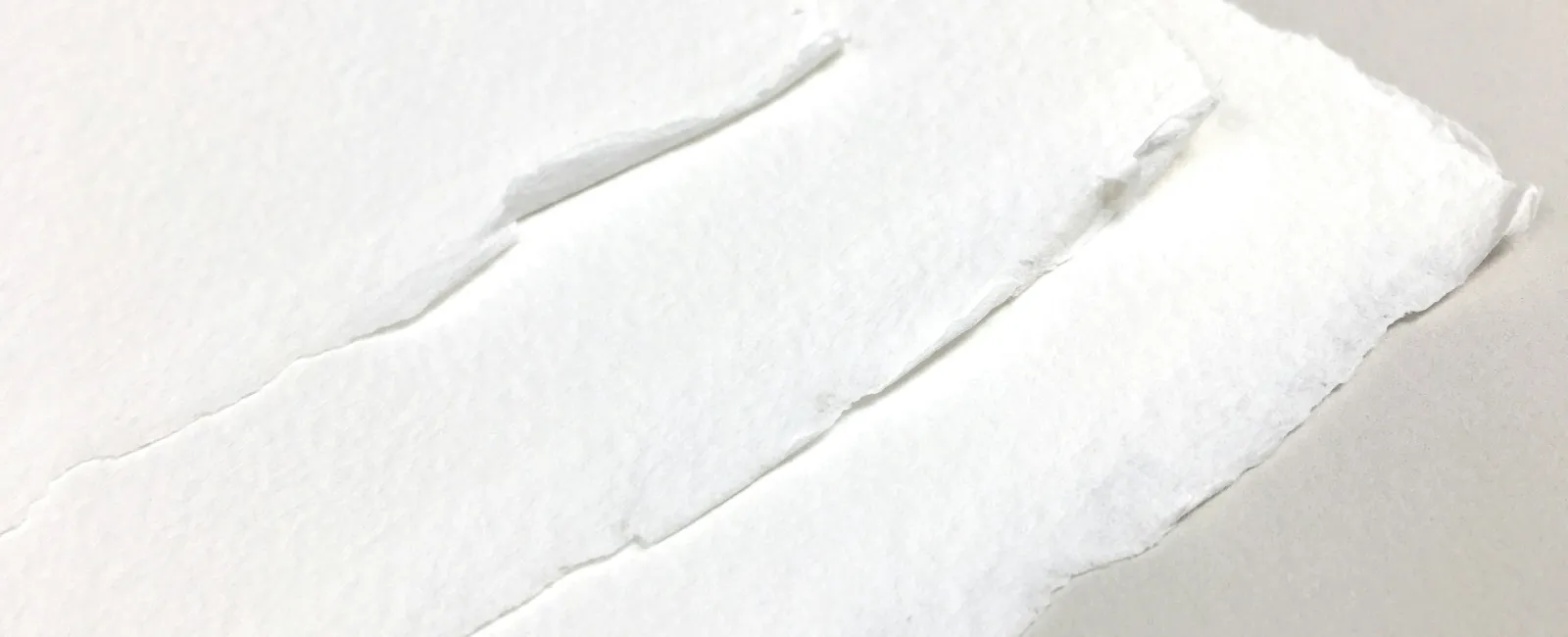 Close-up of textured white torn paper edges layered on a neutral background with soft lighting.