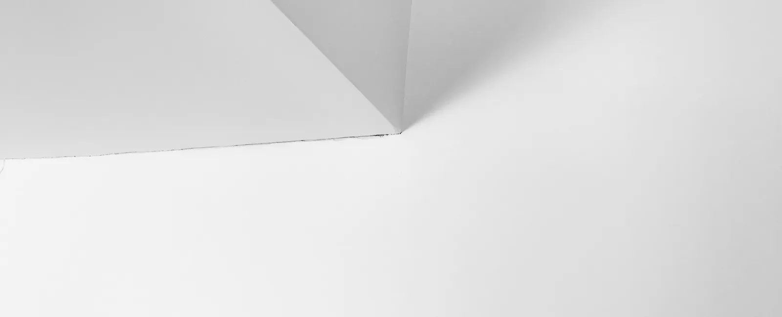 Minimalist corner of a white ceiling with sharp lines and soft shadows creating geometric shapes.