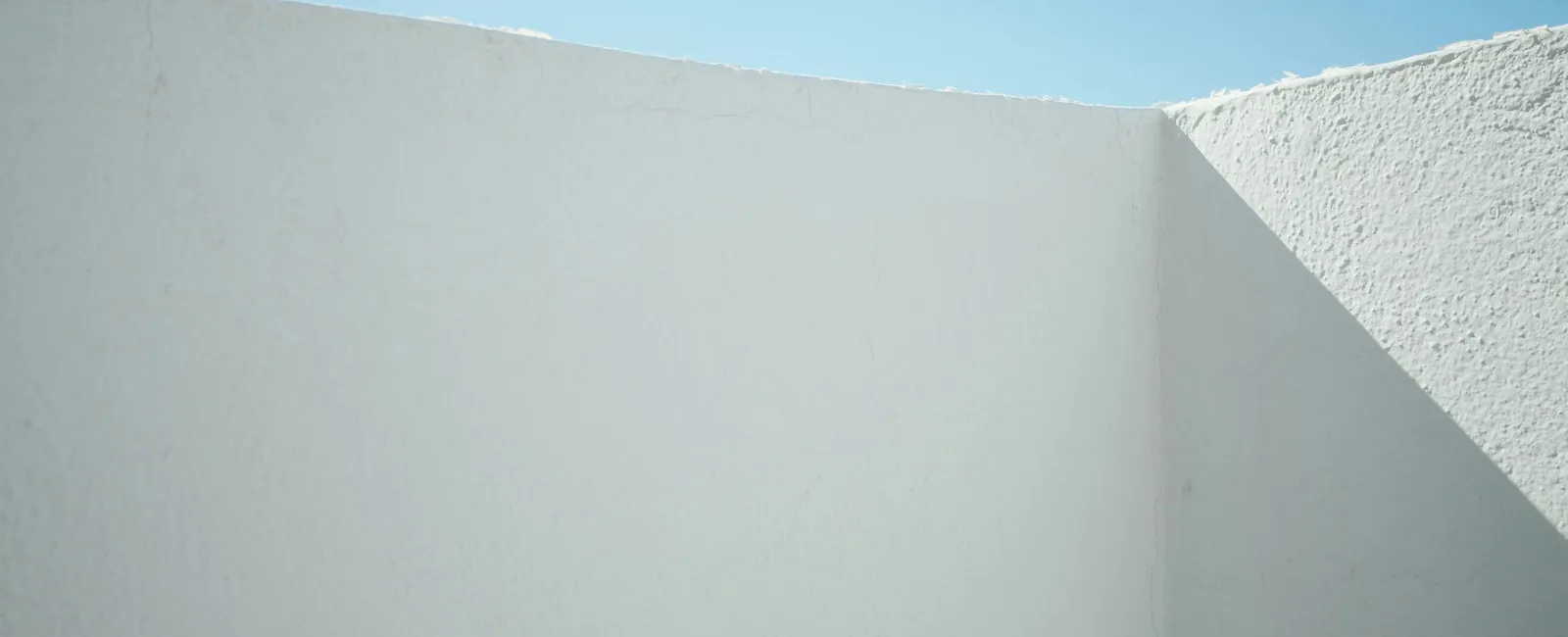 Minimalist white stucco walls casting sharp shadows under a clear blue sky on a sunny day