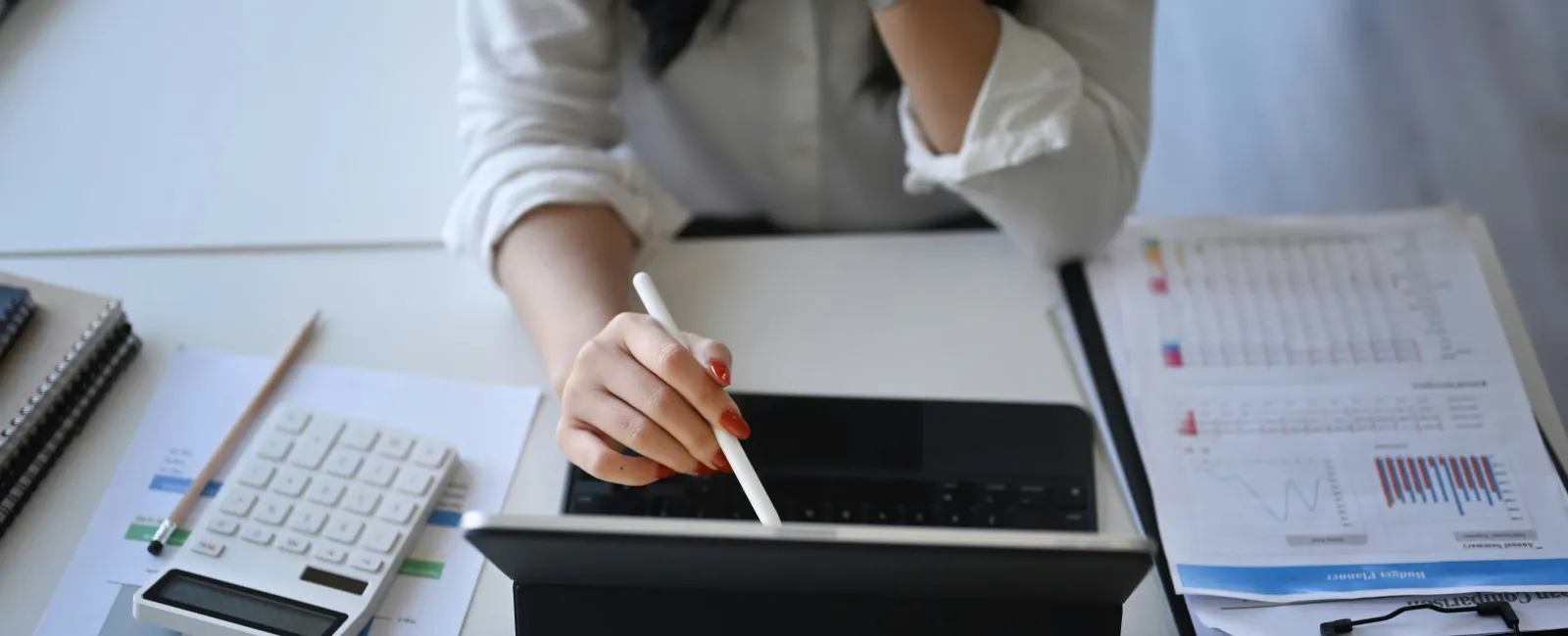 Person using a stylus on a tablet at a desk with PII documents, calculator, and notepads.