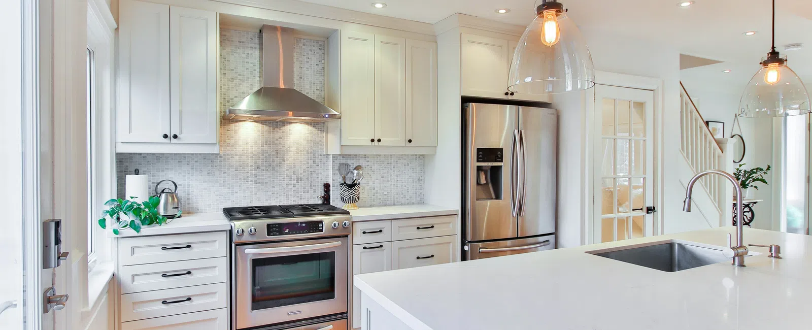 Bright modern kitchen with white cabinets, stainless steel appliances, large island, and pendant lights.