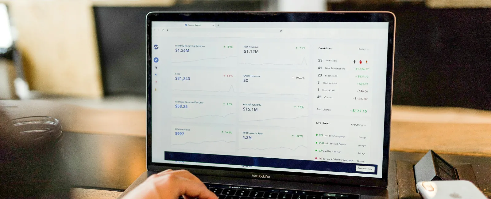 Person analyzing financial data and metrics displayed on a MacBook Pro laptop screen in a cozy workspace.