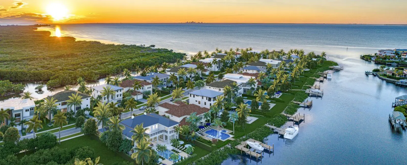 Aerial view of waterfront luxury homes with pools and boats at sunset near a mangrove forest.