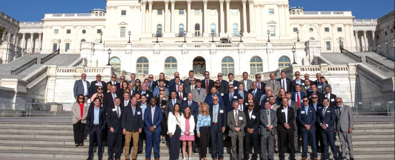 Group photo of diverse individuals in front of the United States Capitol building on a sunny day.