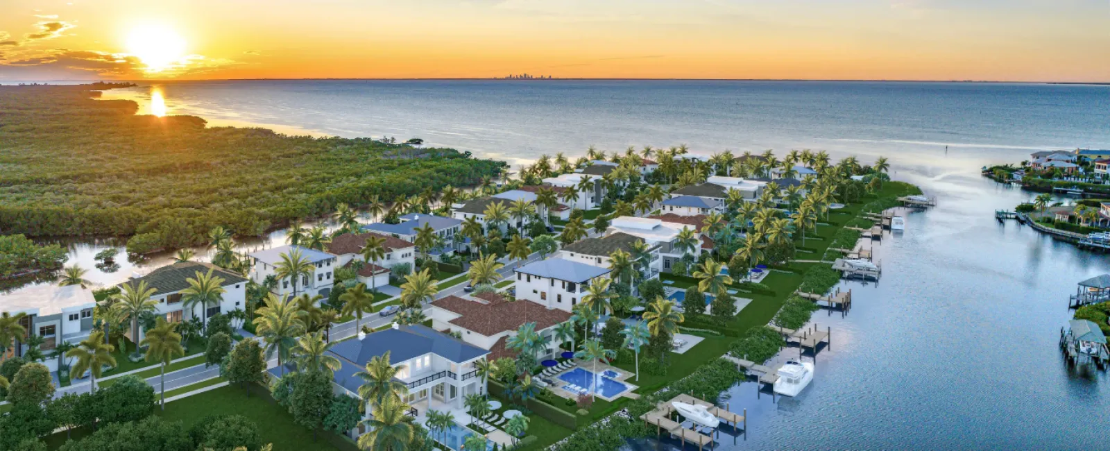 Sunset over modern waterfront homes with palm trees and boats along a canal near the ocean coastline.