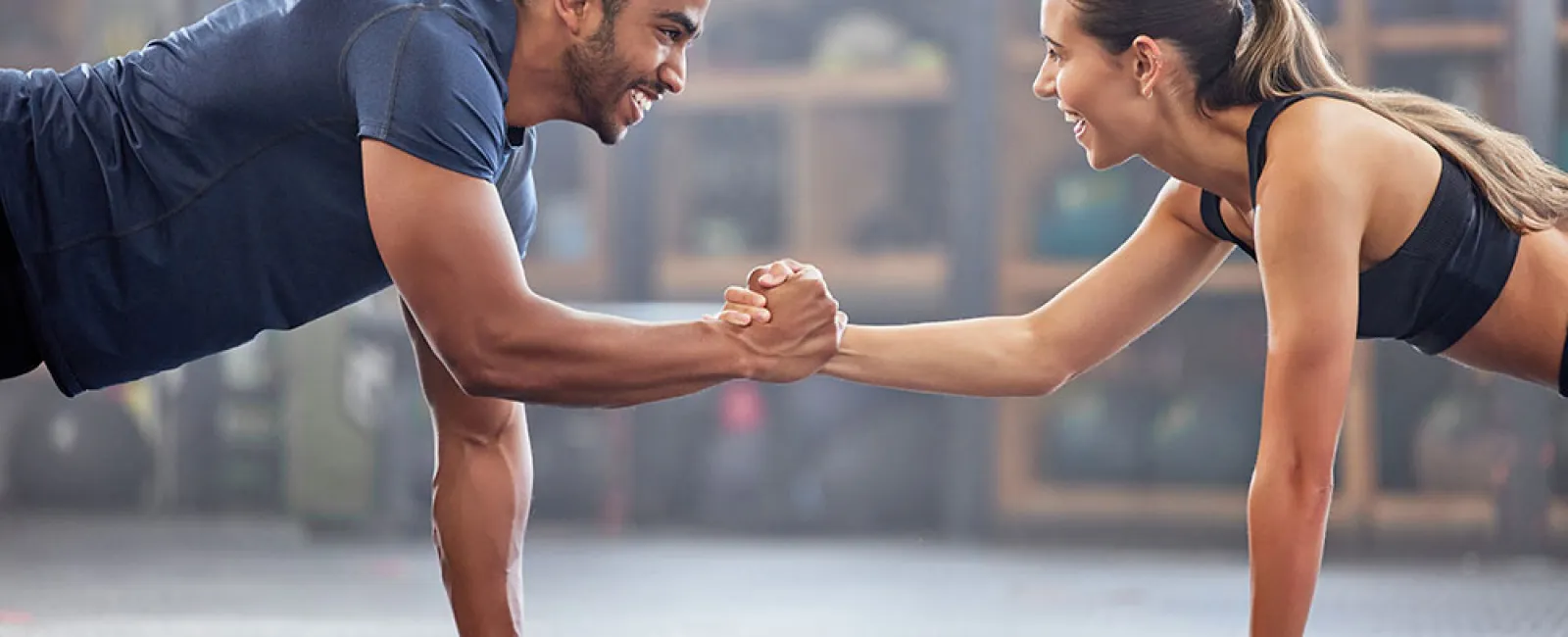 Man and woman doing plank exercise while shaking hands, smiling and working out together indoors.