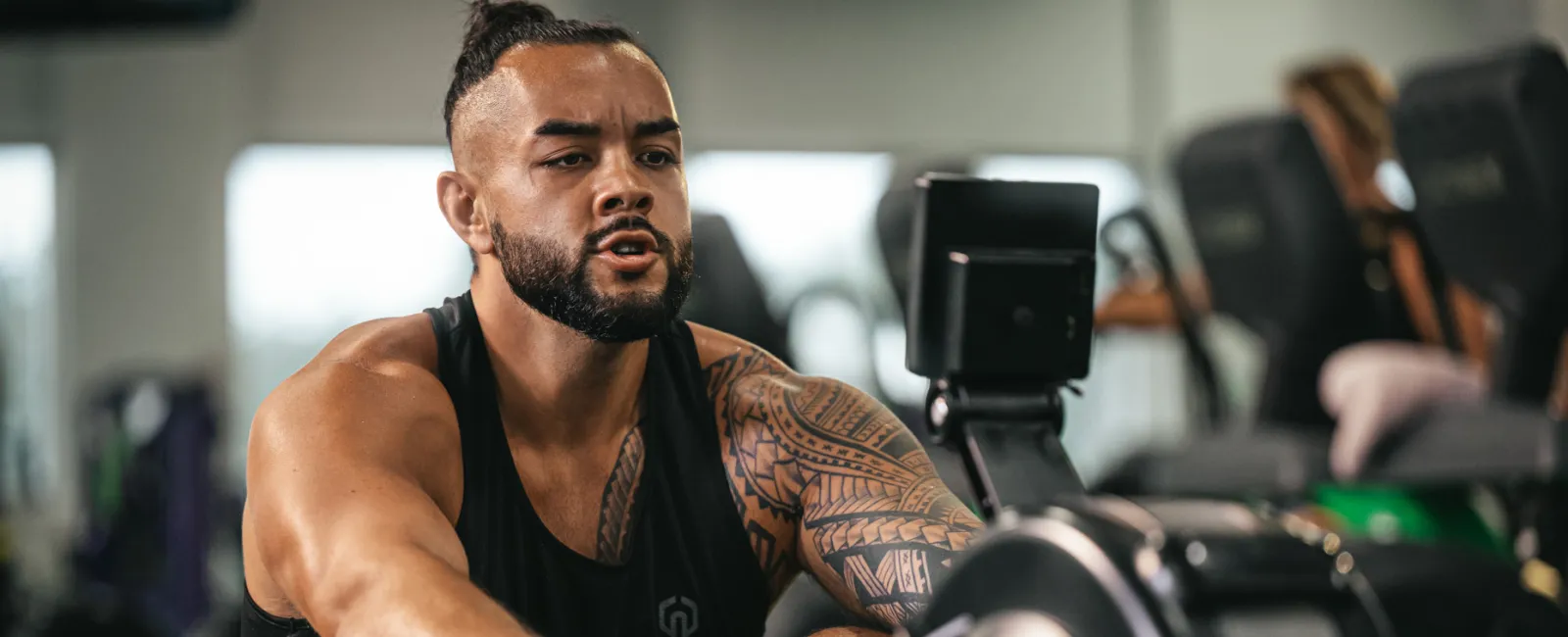 Muscular tattooed man using rowing machine in gym focused on intense workout session.