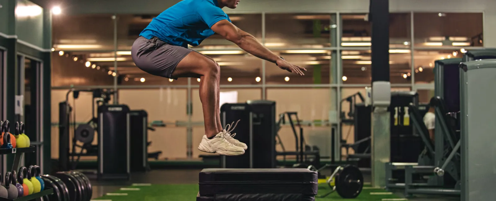 Athlete performing a box jump in a modern gym with fitness equipment and green turf flooring