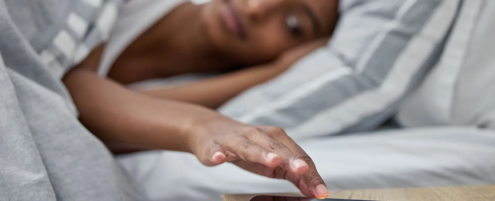 Woman in bed reaching to turn off alarm on smartphone on bedside table early morning