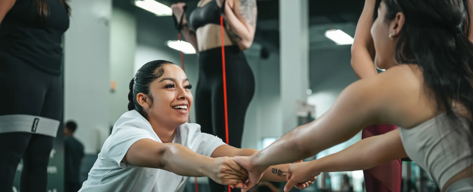 Group of women exercising together in a gym, stretching and using resistance bands with smiles and teamwork.