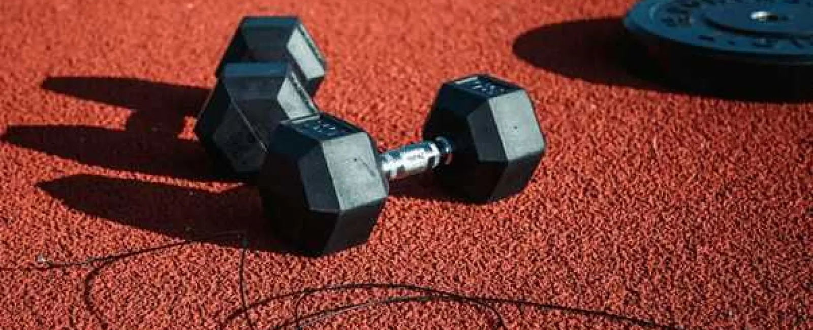 Black hex dumbbells and weight plates on red textured gym floor with exercise resistance cords.