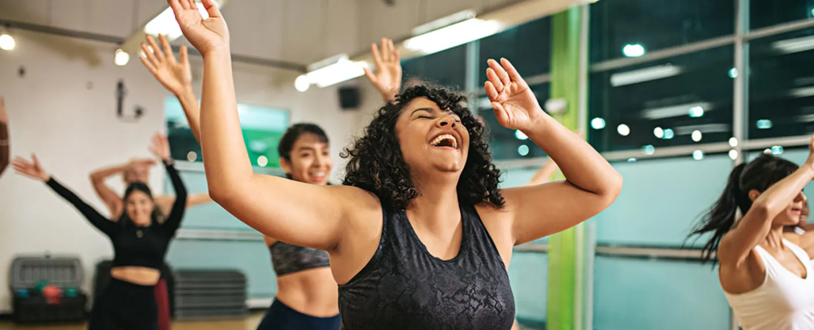 Diverse women enjoying an energetic group fitness dance class in a bright studio with mirrors and wooden floors.