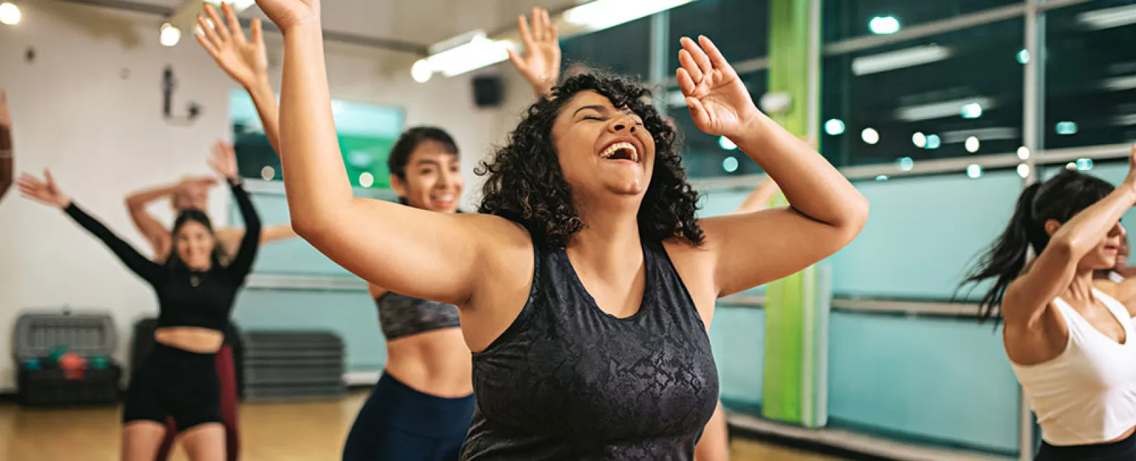 Happy diverse women dancing energetically in a bright fitness studio group exercise class with raised arms.