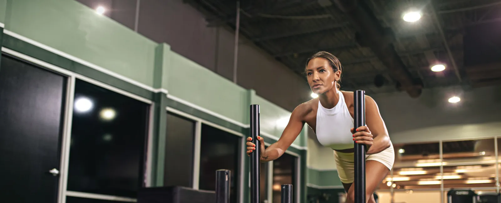 Woman in white athletic wear pushing a weighted sled on green turf in a gym setting.