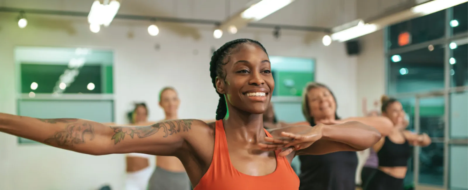 Smiling woman in an orange sports outfit leading a diverse group in an exercise class in a studio.