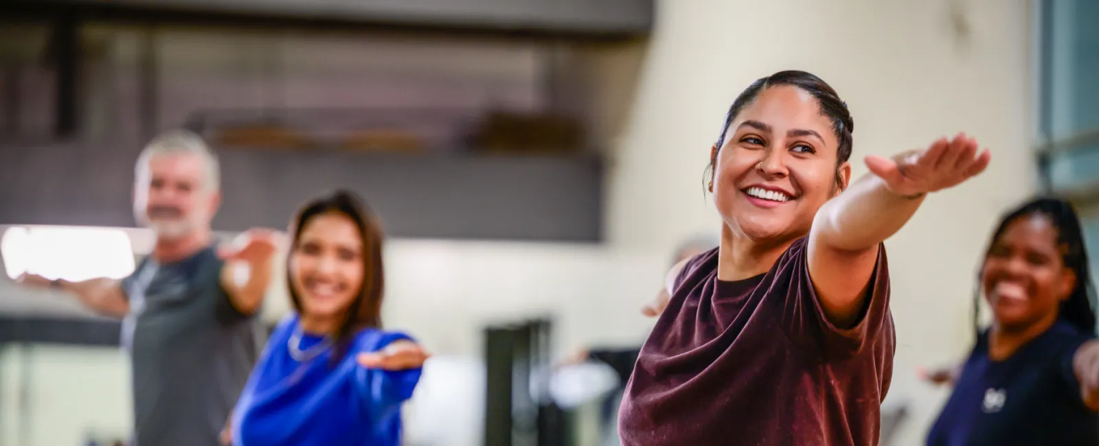 Group of diverse adults smiling and stretching arms forward during a fitness class in a bright gym studio