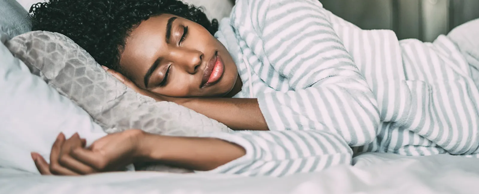 Peaceful young woman sleeping on bed with striped pajamas and soft pillows in cozy bedroom