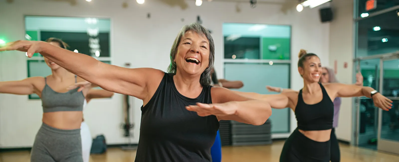 Happy diverse group of women enjoying a fitness dance class in a bright gym studio with wooden floors.