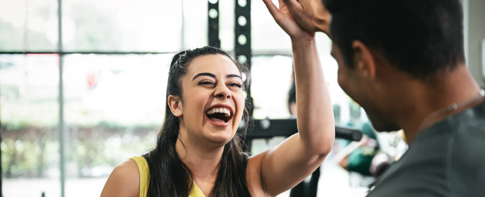 Smiling woman in yellow tank top giving a high five to a man at the gym.