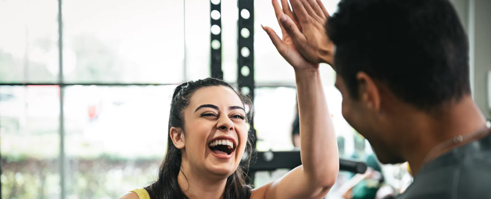 Smiling woman in yellow tank top giving a high five to a man at the gym.