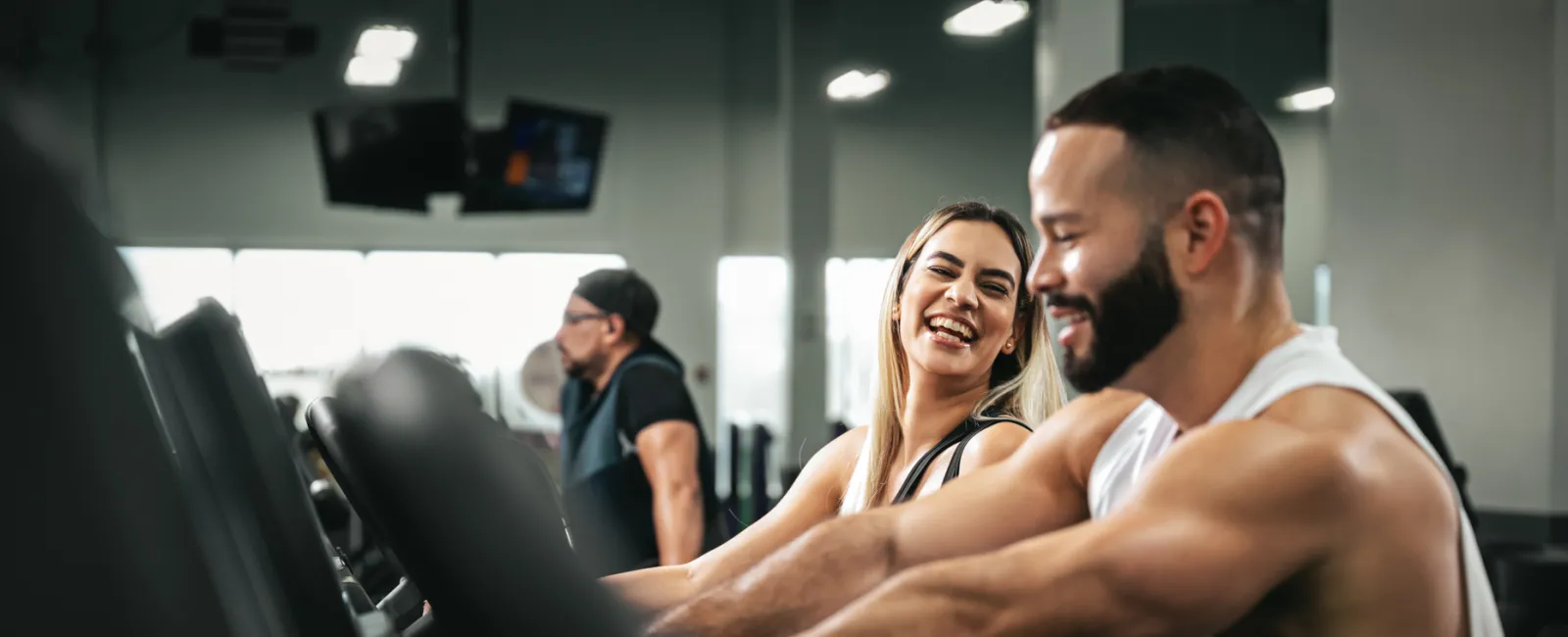 Happy young man and woman exercising together on cardio bikes in a gym setting