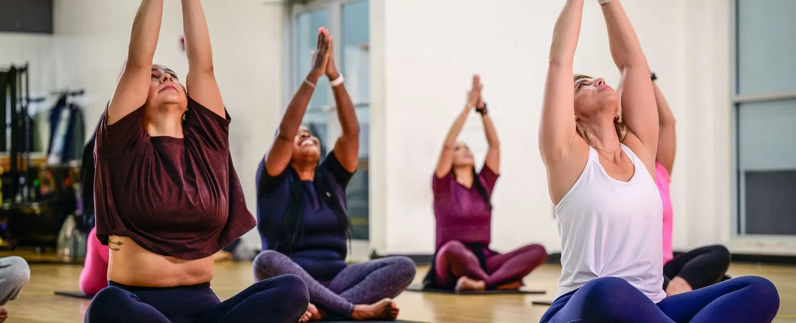 Group of women practicing seated yoga with arms raised in a bright studio