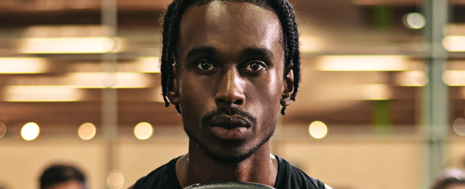 Determined man lifting a kettlebell during a gym workout with blurred people and lights in the background