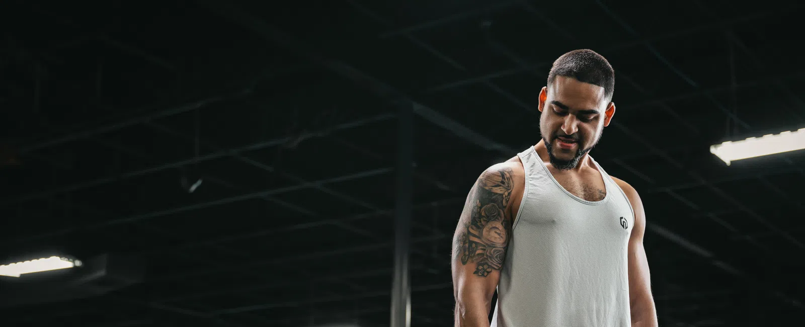 Man lifting dumbbells in YouFit Gyms wearing a white tank top and green pants under bright lights