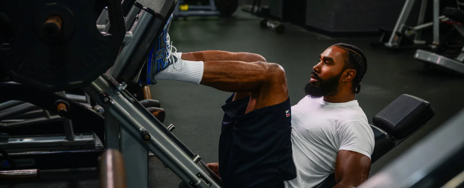 Man with beard and white shirt working out on a leg machine in YouFit Gyms.