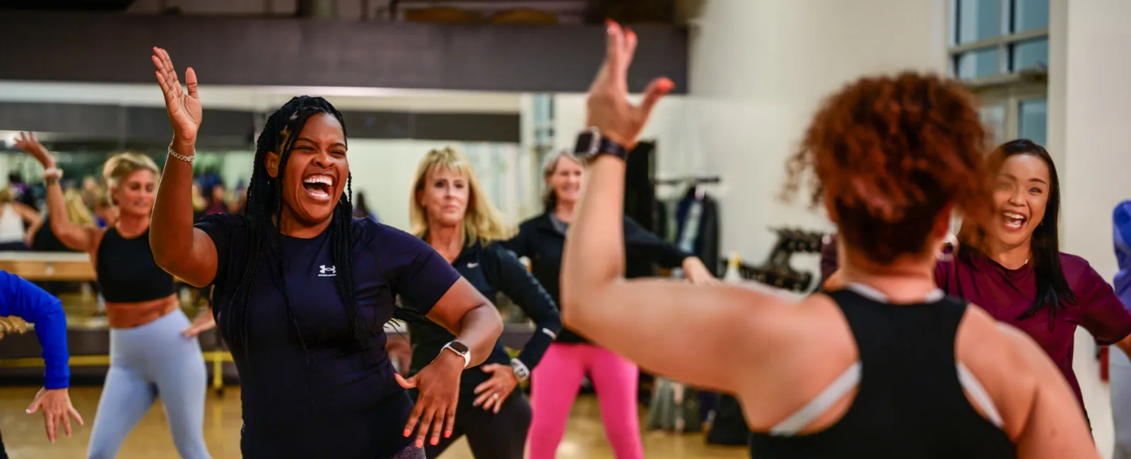 Diverse group of women enjoying a lively dance fitness class in a bright gym studio.