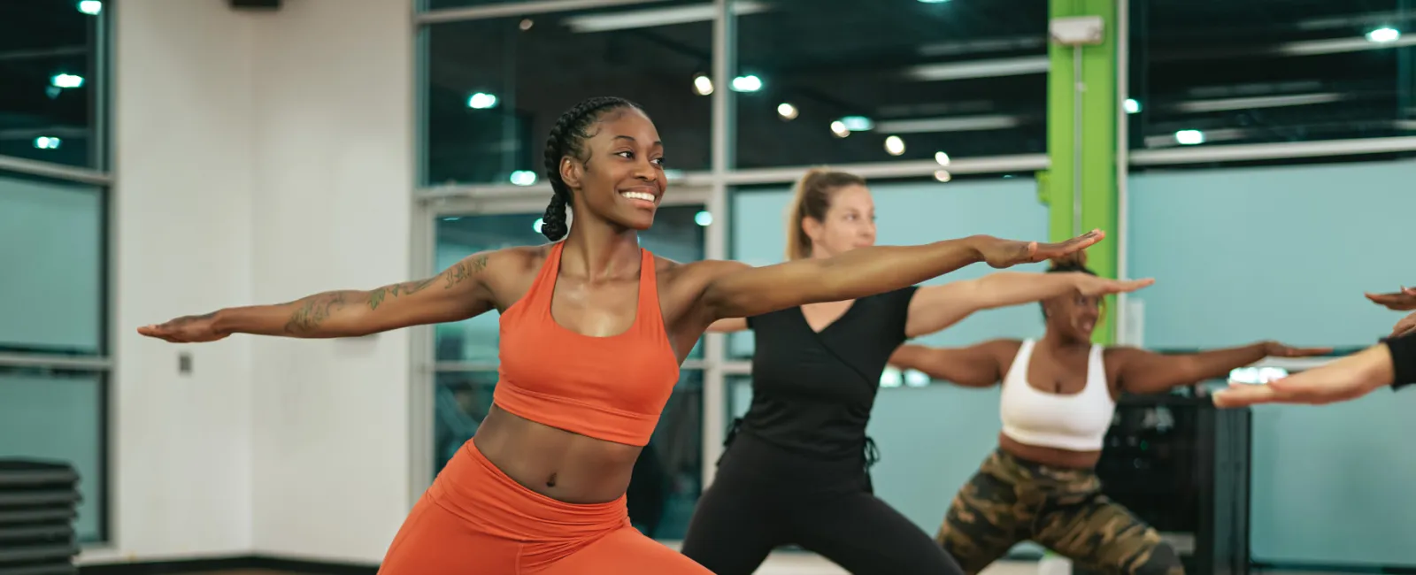 Group of diverse women practicing yoga warrior pose in bright fitness studio with mats on wooden floor
