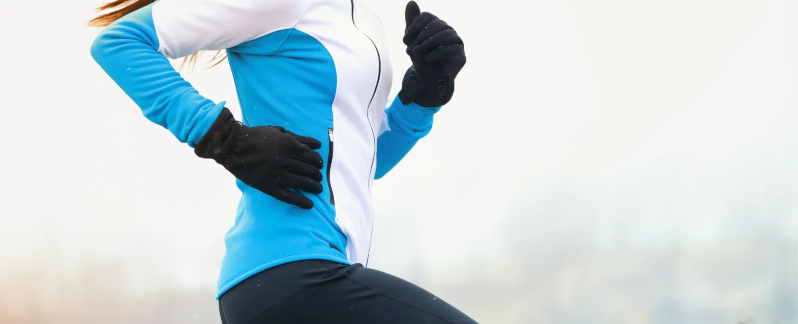 Woman running outdoors in winter gear with gloves and a blue and white jacket on a cold day