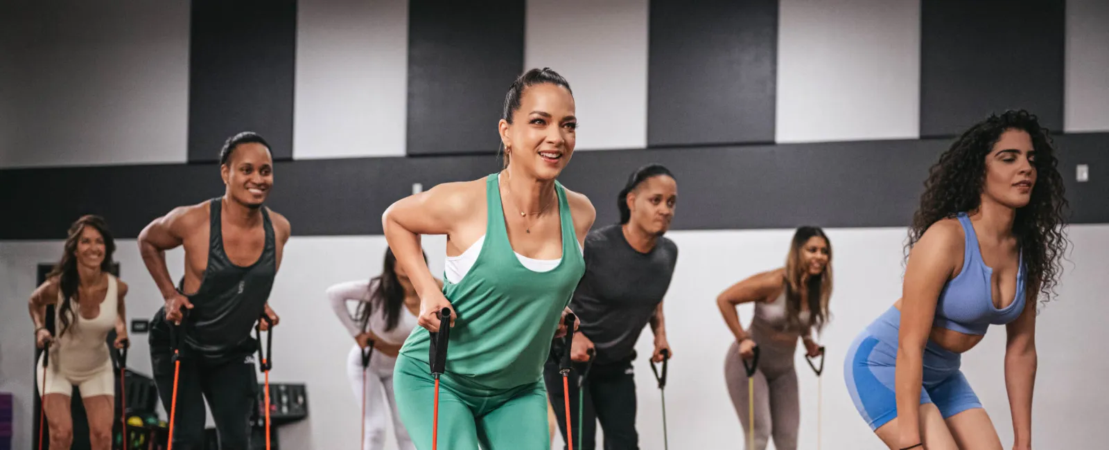 Group of diverse women exercising with resistance bands on step platforms in a fitness class studio.