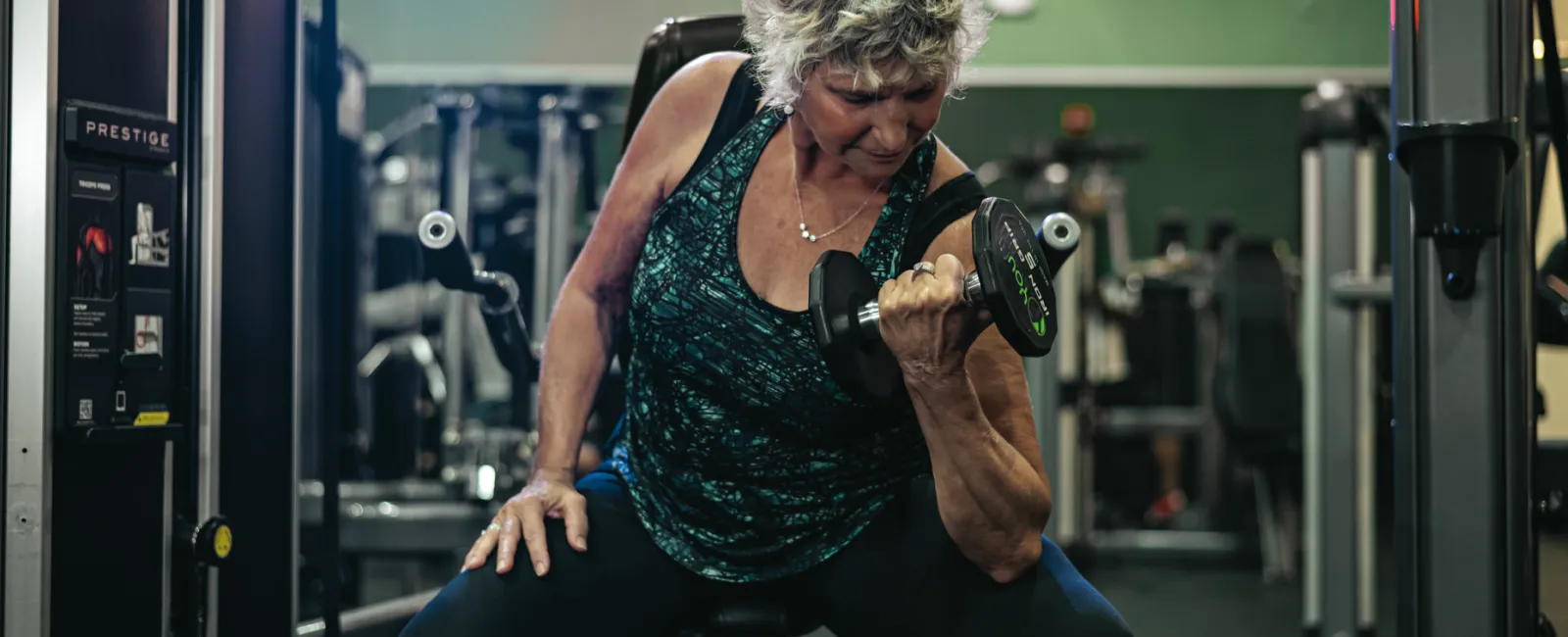 Mature woman lifting a dumbbell seated on gym equipment focusing on strength training.
