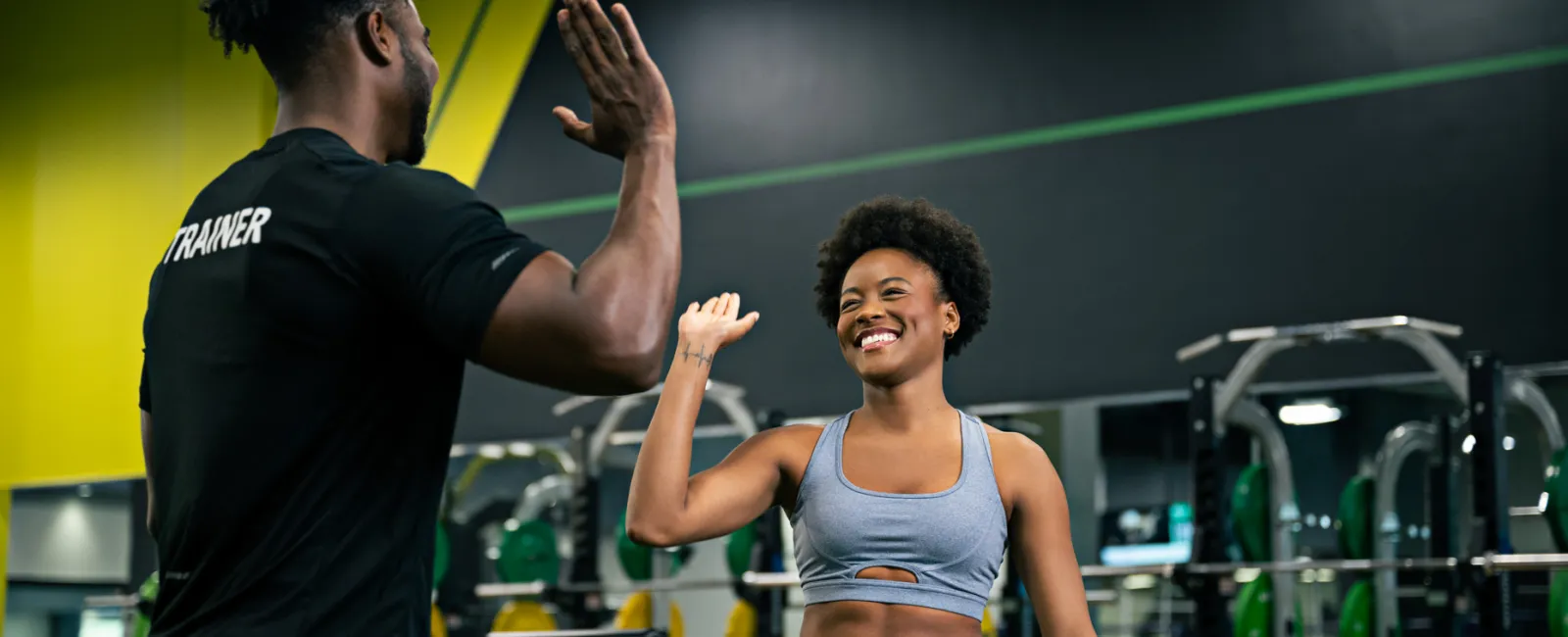 Female athlete and male trainer exchanging a high-five in a colorful gym setting with fitness equipment.