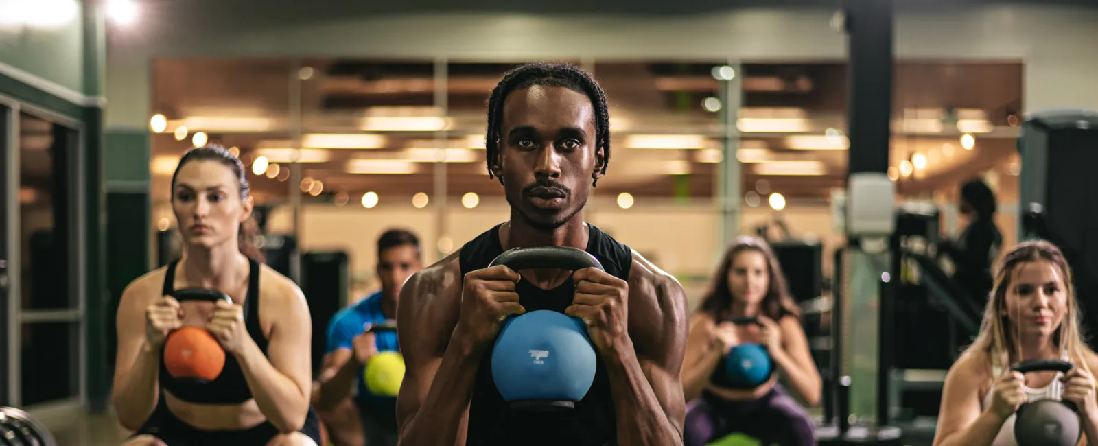 Group of diverse people doing kettlebell squats together in a gym with green turf flooring