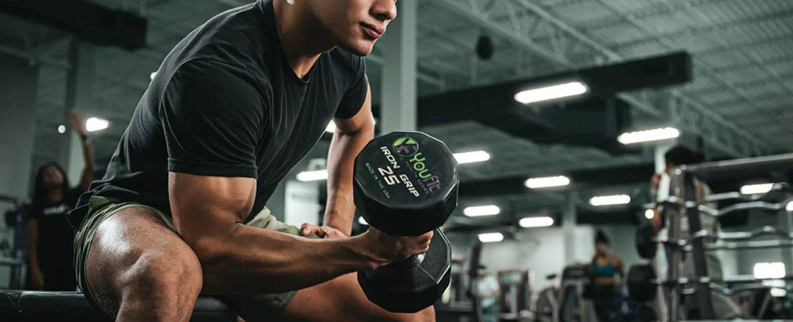 Man lifting a 25-pound dumbbell focused on bicep curls in a gym setting with equipment in the background