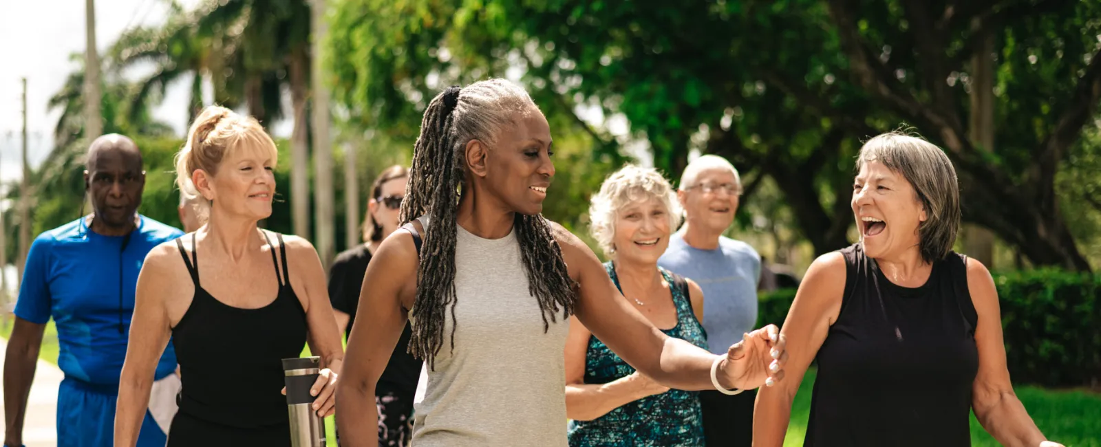 Group of diverse seniors happily walking outdoors in activewear holding water bottles and chatting.