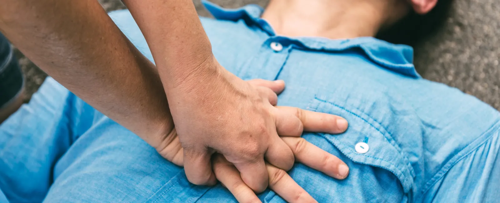 Close-up of hands performing CPR chest compressions on a person lying on the ground wearing a blue shirt