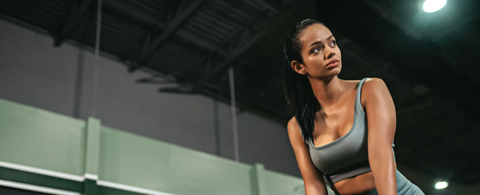 Fit woman in gray workout clothes using battle ropes in a gym with large windows and high ceilings
