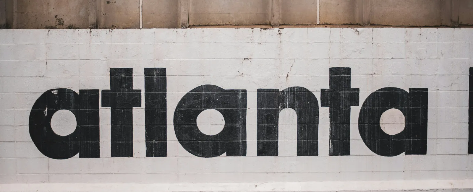 Black bold text reading atlanta painted on a white brick wall under a concrete section.