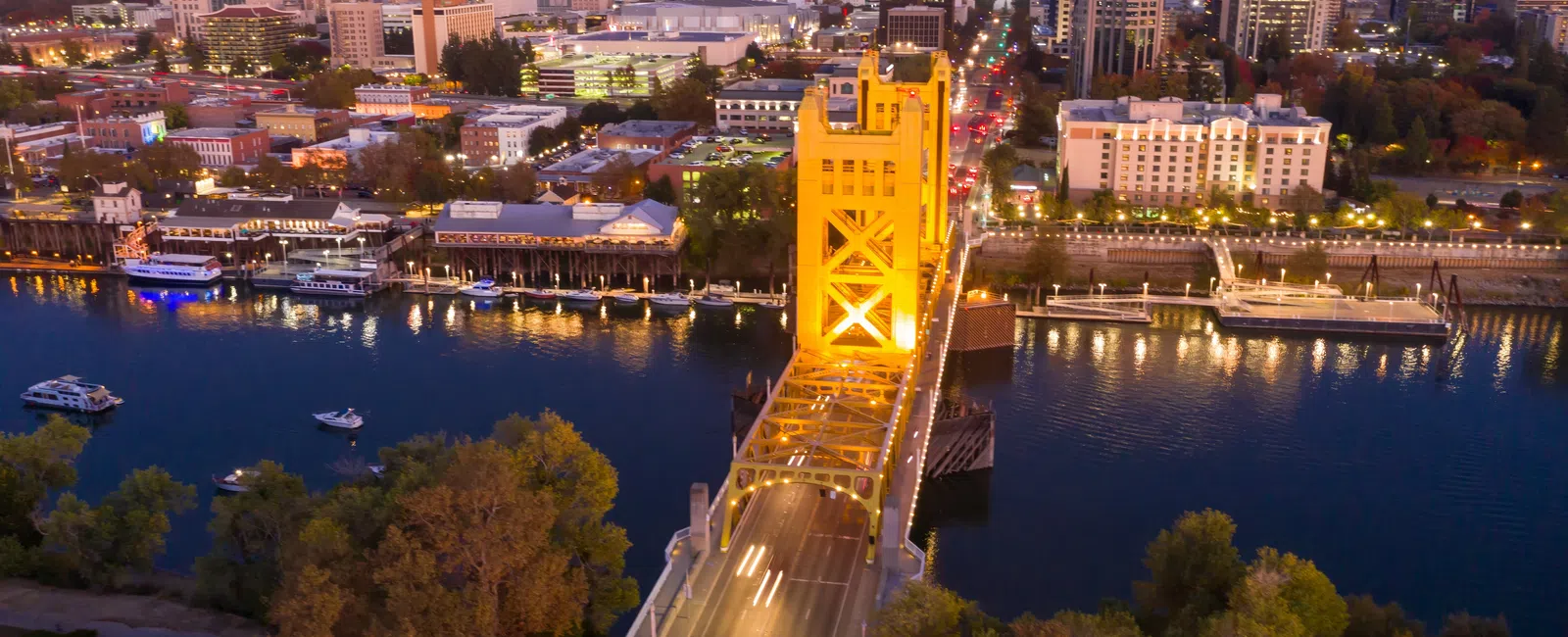 Golden Tower Bridge illuminated at dusk with city skyline and river in Sacramento, California.