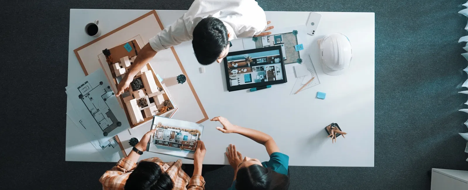 Three professionals collaborate over architectural plans and a building model on a white table in a modern office.