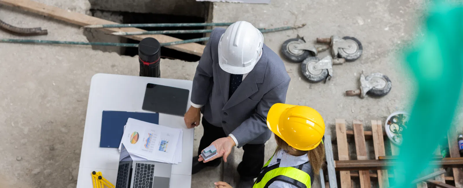 Construction manager and engineer reviewing project plans and data on site with laptop and documents.