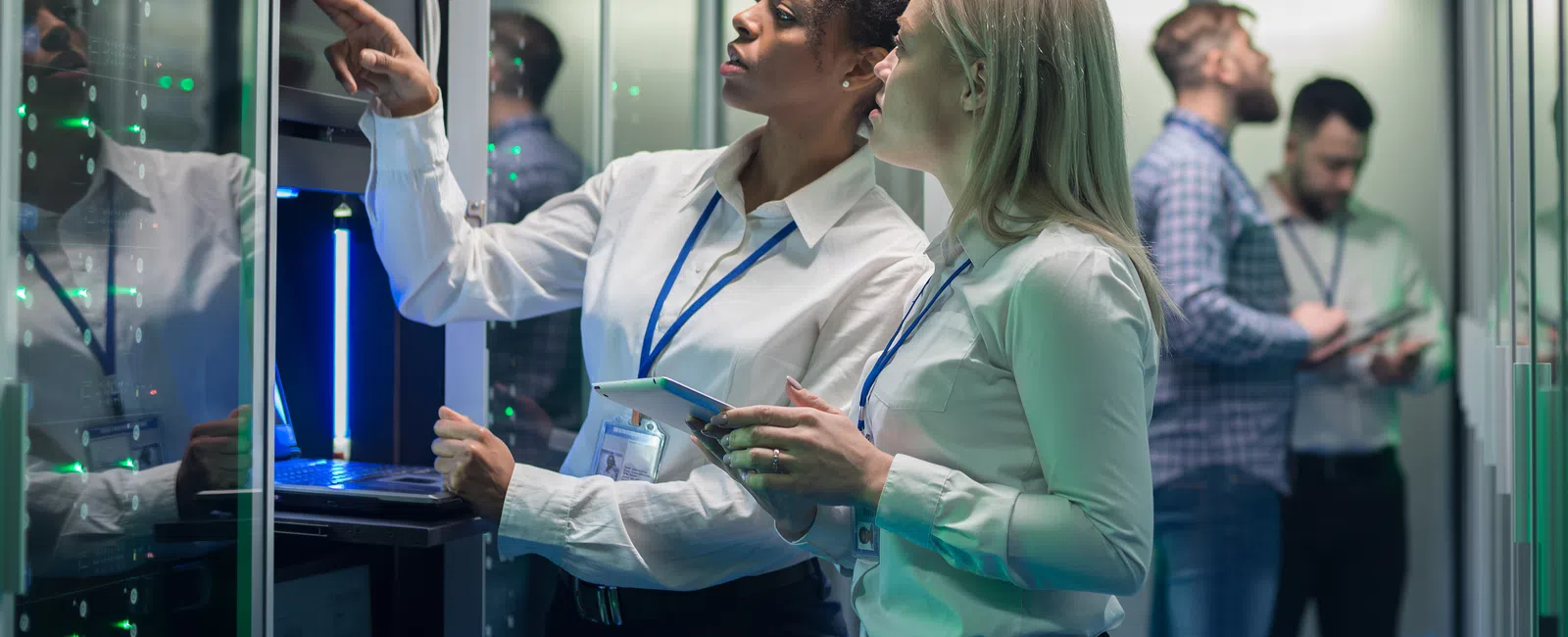 Two IT professionals inspecting server hardware in a data center with two men working in the background.
