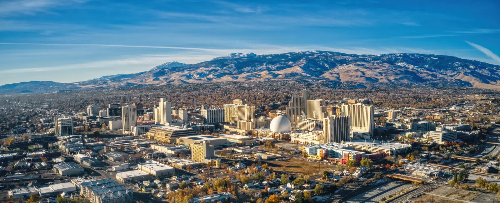 Aerial view of a city with urban buildings, bridges, and mountainous background under a clear blue sky.