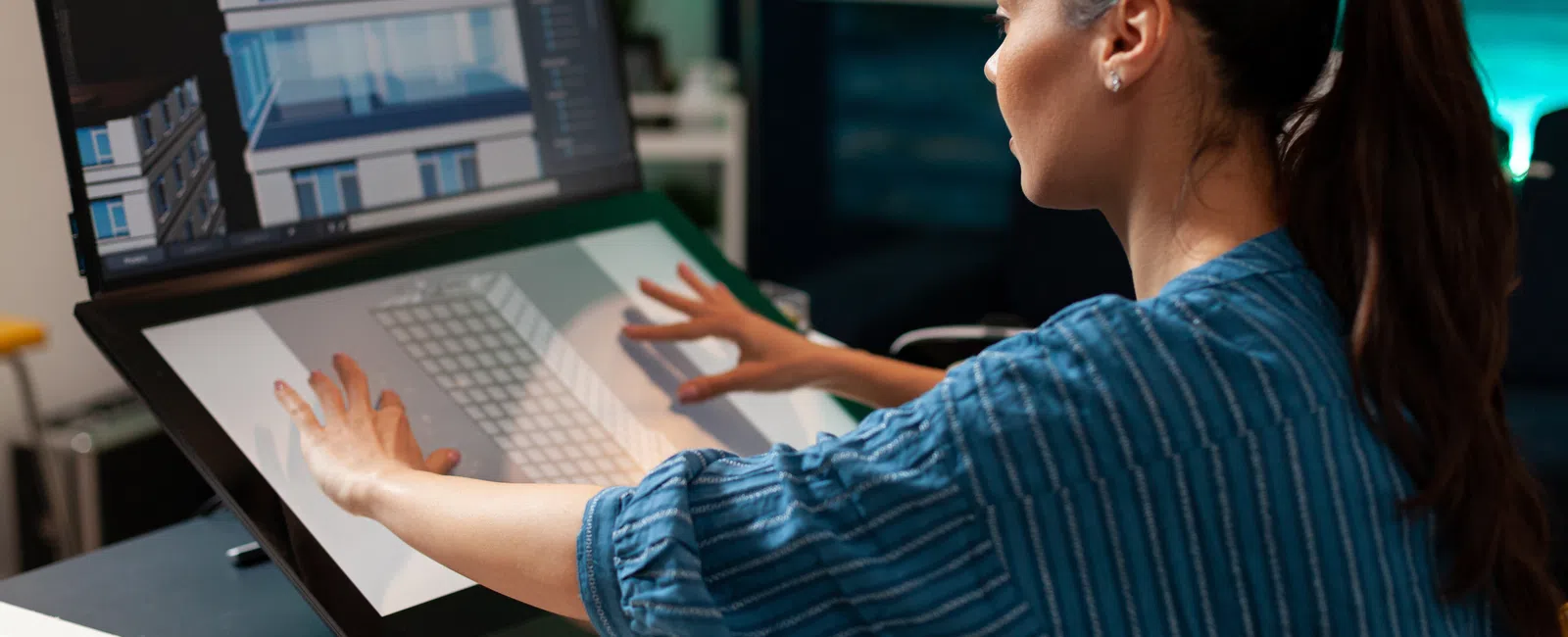 Woman using a large touchscreen monitor to design a building facade in a modern office at night